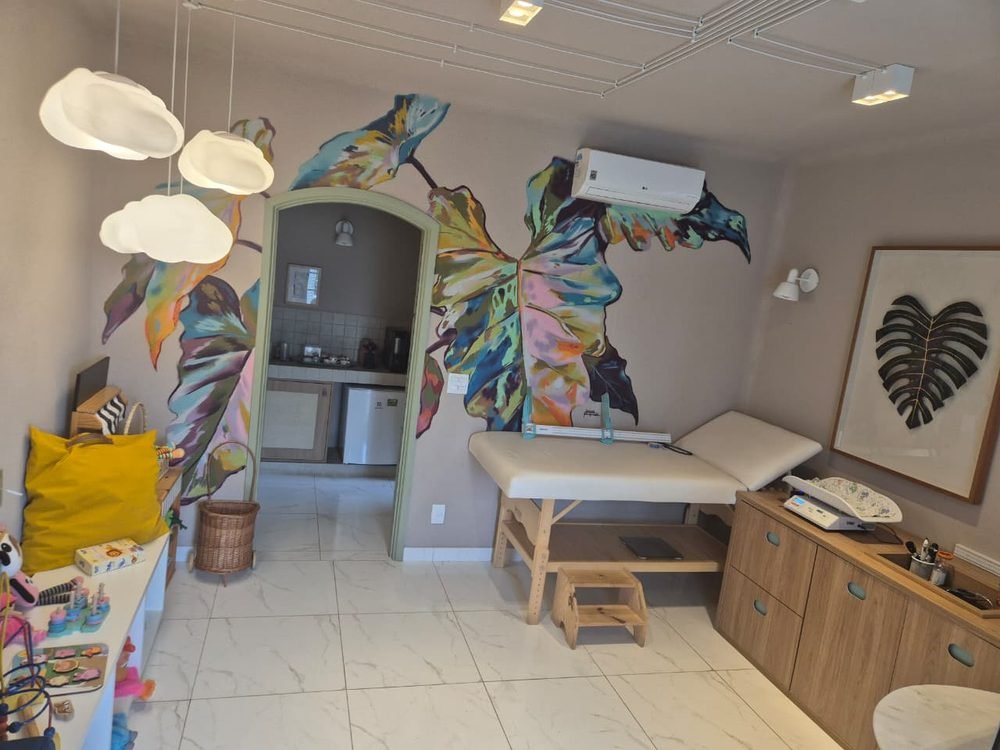 Consultório da Dra. Rhayany com maca infantil e mural colorido de folhas na parede