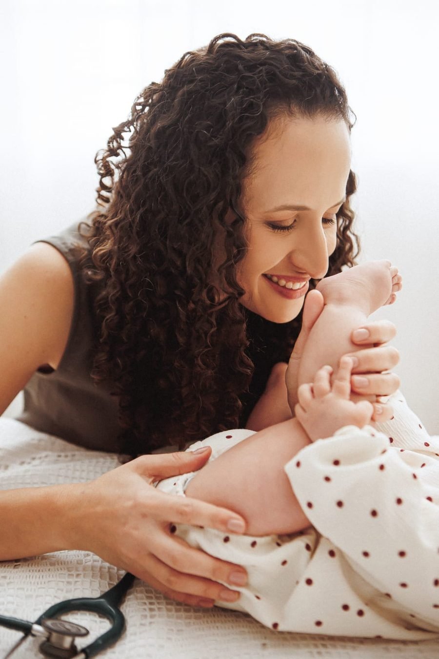 Dra. Rhayany sorrindo com carinho enquanto segura os pezinhos de um bebê