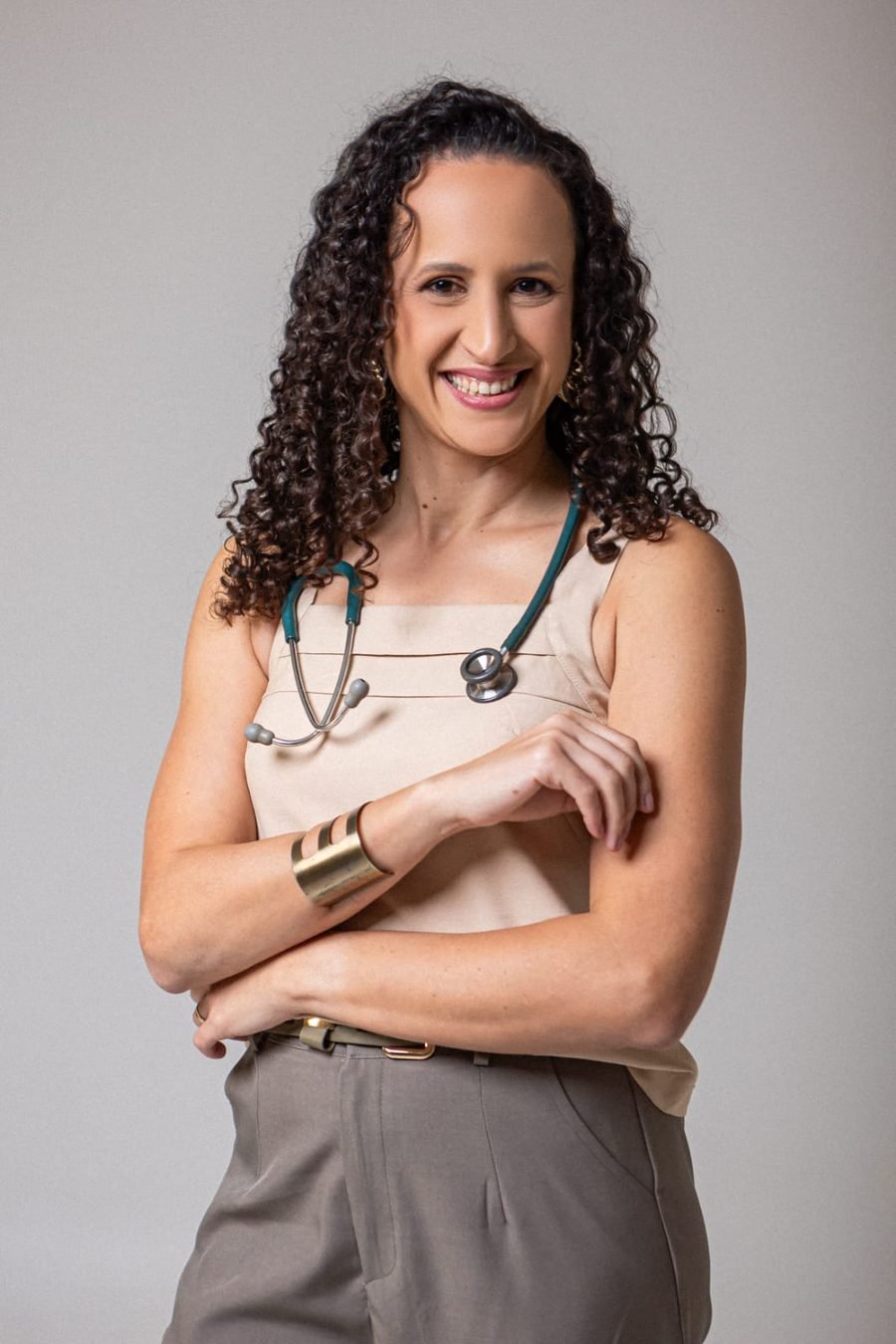 Dra. Rhayany Barbosa em pé, sorrindo, com estetoscópio verde no pescoço